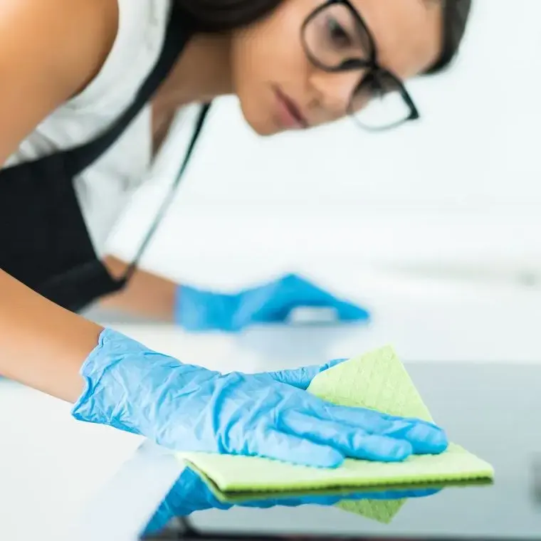 Reinigungskraft mit Handschuhen reinigt eine Arbeitsfläche
